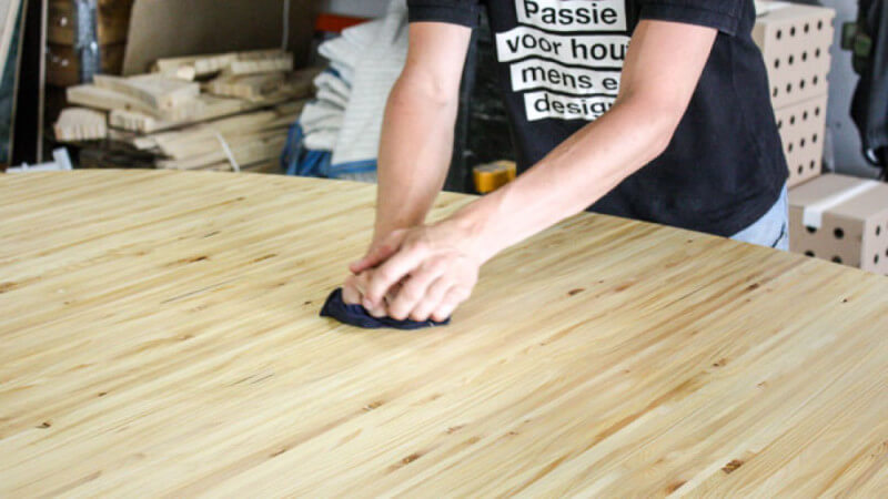 A man cleaning a table top finished with Oil Plus 2C.