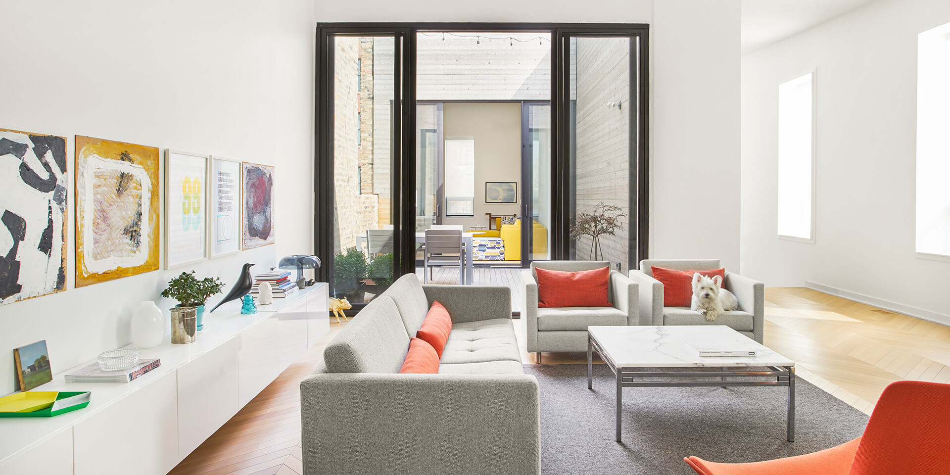 Dog lounges on the couch in beautiful modern apartment featuring a chevron style white oak floor.