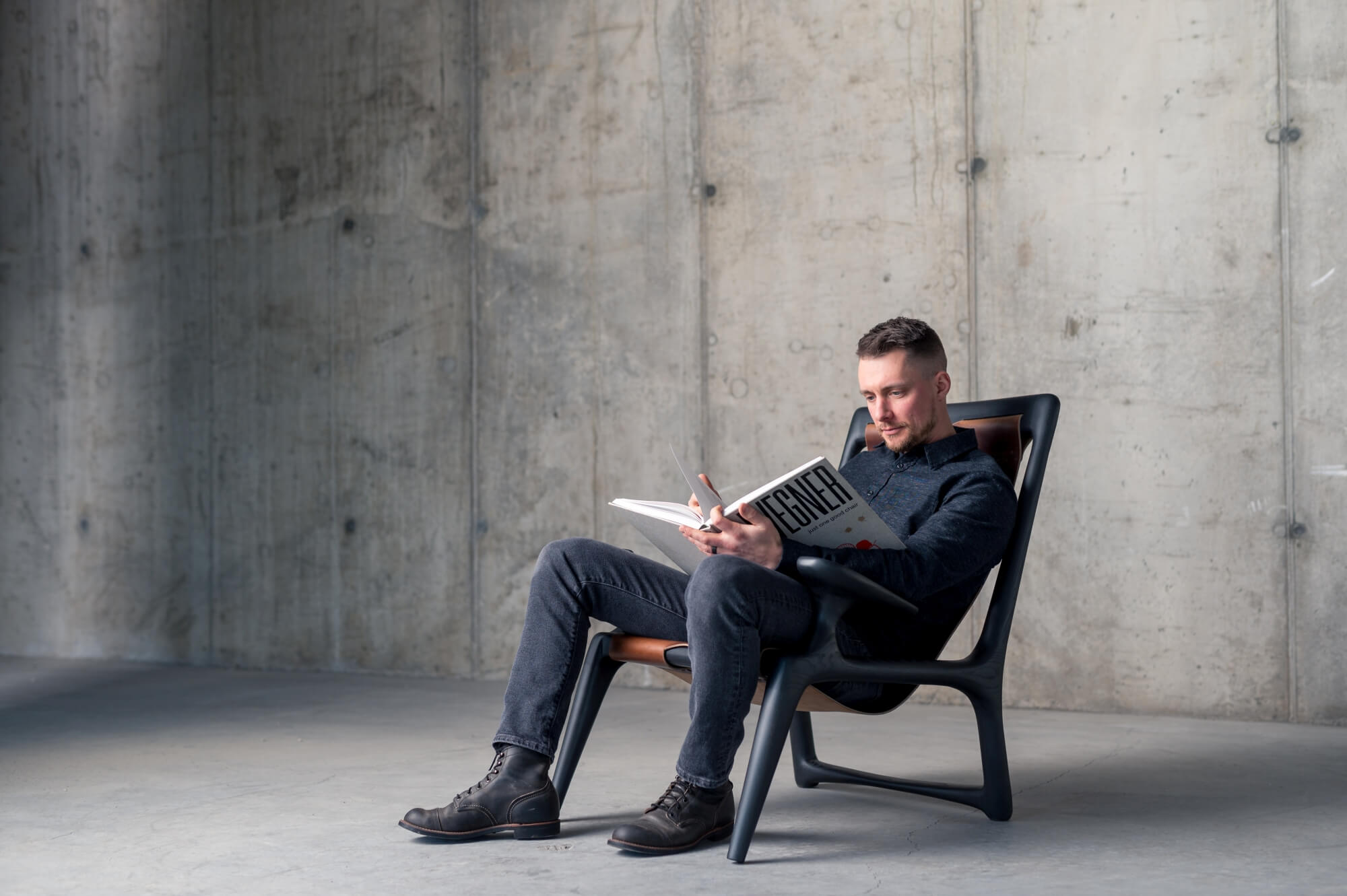 Man sitting in custom wood and leather chair reading a book.