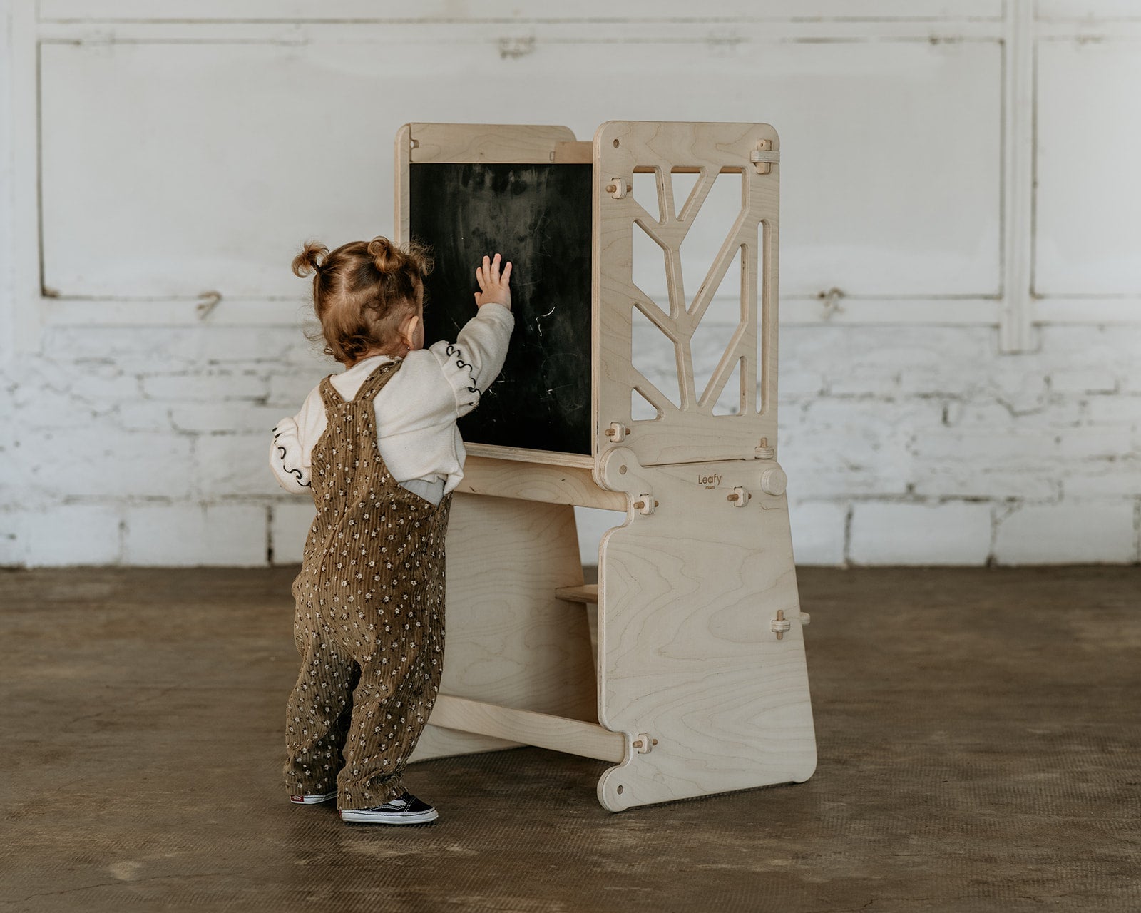 A child stand at the chalk board side of the toddler learning tower.