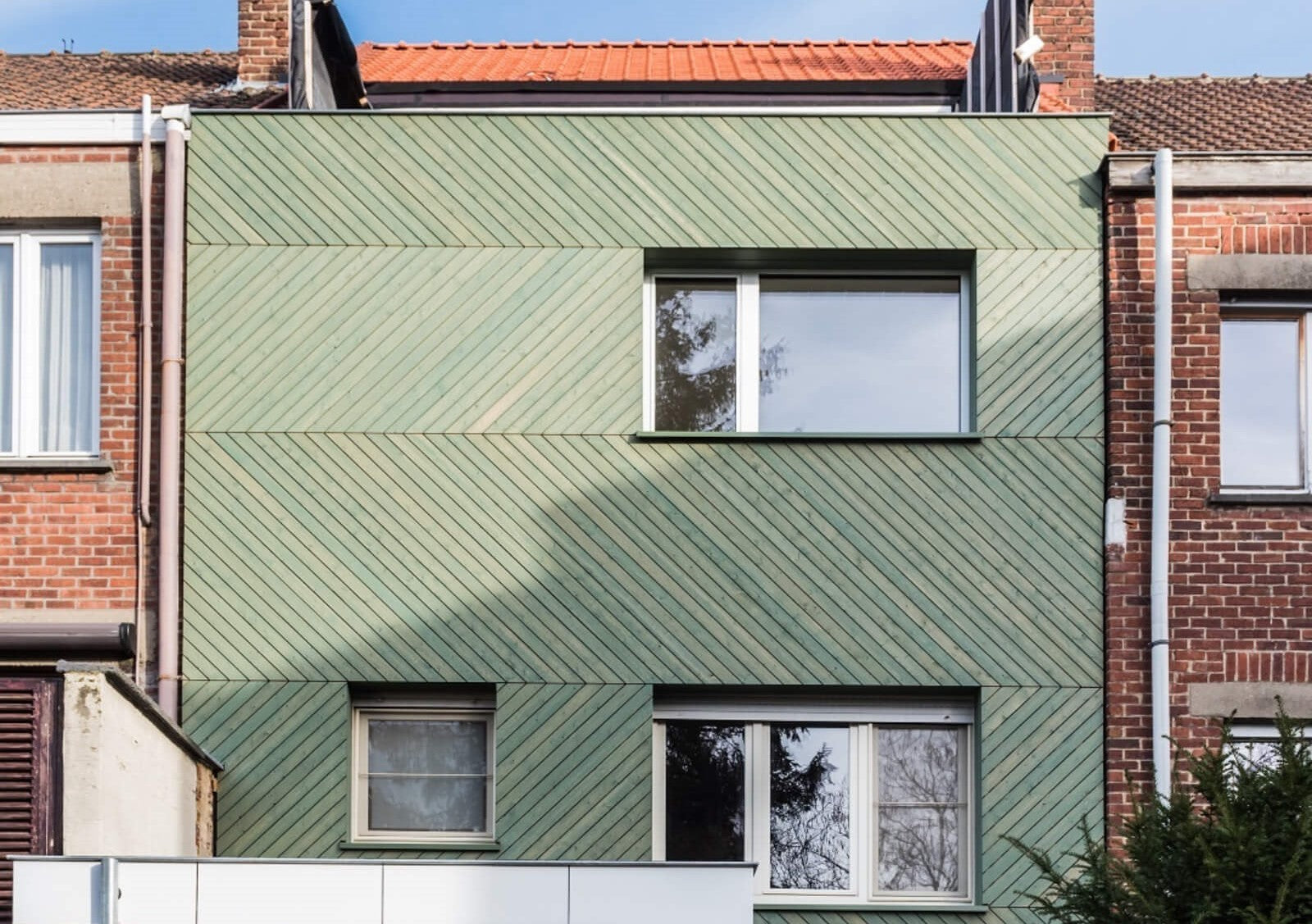 A building with green wood siding finished with Rubio Monocoat WoodCream. Two brick adorned buildings sit on either side of it.