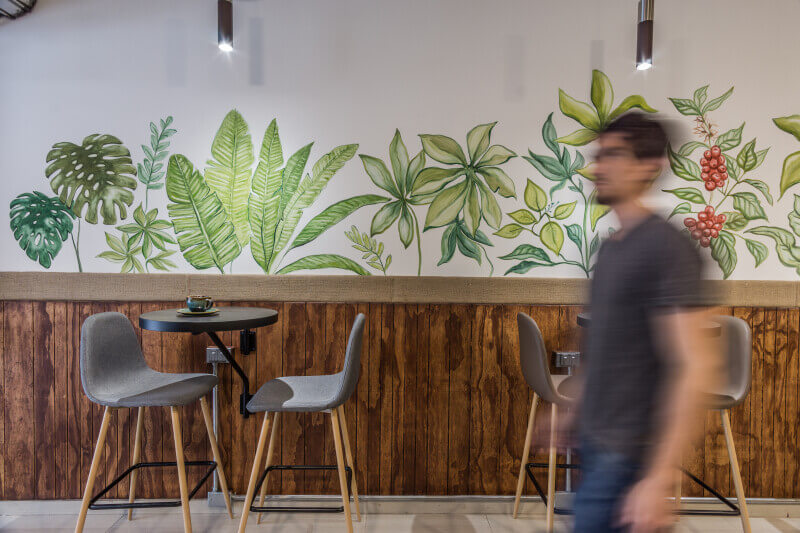 An out of focus man walking in the foreground with a trendy styled coffee shop interior in the background.