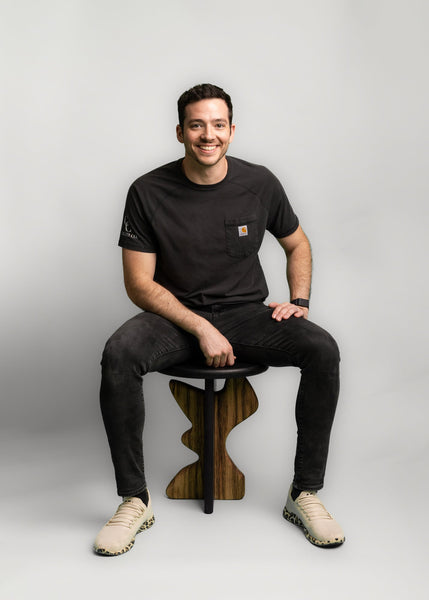 A man is sitting on a side table made from white oak and black limba wood.