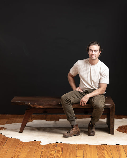 A man is sitting on a live edge walnut coffee table that featured maple bow ties and a waterfall edge.